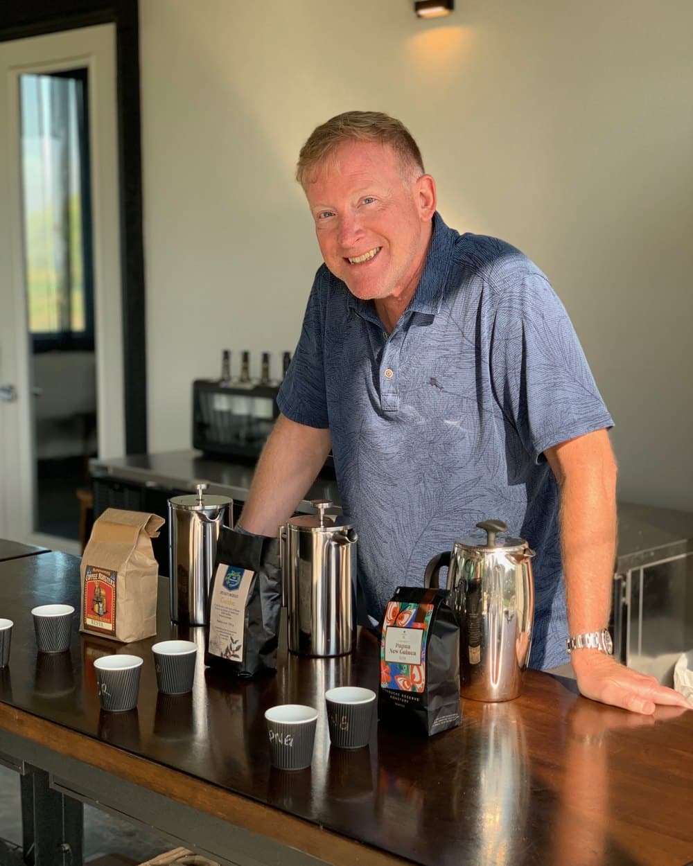 John Shepard behind a counter set with coffee presses, smiling.
